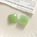 Macro detail of two light green resin square beads on a vintage newspaper background - Green