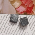 Détail de boucles d'oreilles carrées en résine avec texture fumée et craquelée sur un magazine - Gris fumé