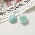 Détail de breloques de boucles d'oreilles en résine vert clair marbrée sur journal - Carré / Bleu