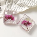 Dettaglio macro di ciondoli quadrati in resina fatti a mano con fiori secchi rosa e foglia d'argento - Viola Rosa