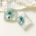 Dettaglio macro di ciondoli in resina quadrati con fiori secchi blu e foglia argento - Verde Lago