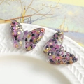 Macro detail of transparent resin butterfly charms with pink and gold glitter flakes - Purple