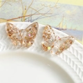Close-up of clear glitter resin butterfly charms with gold sequins on ceramic plate - Nude Pink