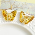 Close-up of transparent resin butterfly accessories with sparkling gold sequins on white ceramic - Gold