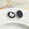 Makro-Detail von Vintage Harz Oval Charms mit weißem Schmetterlingsrelief auf mattem Schwarz - Schwarz