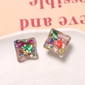 Dettaglio macro di ciondoli quadrati in resina con scaglie iridescenti su piatto ceramico - Stile Quadrato con Foglia Colorata