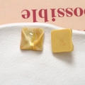 Macro detail of yellow resin earrings with marble texture and wavy pattern on ceramic tray - Yellow