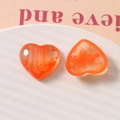 Macro view of orange heart-shaped resin charms with swirl and smoky textures in a tray - Orange