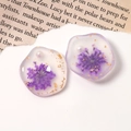 Macro detail of handmade resin earrings with dried flowers, gold foil and pearl accents - Purple