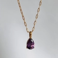 Detail of a large pear-cut purple zircon pendant on a golden paperclip chain necklace - February