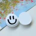 Dettaglio di accessori tondi in resina bianca con un motivo minimalista di faccina nera - Bianco