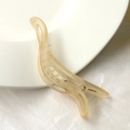 Detailed view of champagne matte hair claw clip on white ceramic plate with twisted design - Khaki