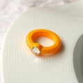 Gros plan d'une bague en acrylique orange avec un diamant incrusté sur un plateau blanc - Orange