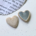Detalle macro del botón de lana sintética en forma de corazón con reverso metálico - Beige