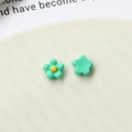 Macro view of mint green acrylic flower charms with yellow center on white ceramic plate - Green