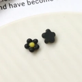 Detailed macro view of black matte floral resin charms with bright yellow centers - Black