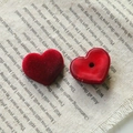 Detailed view of red flocked and resin heart charms on a rustic text-printed fabric - Heart