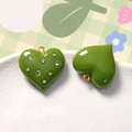 Macro view of green heart resin pendants with inlaid rhinestones and gold rings - Green