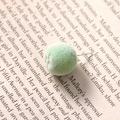 Close-up of a light green flocked spherical earring stud on an artistic book background - Lime Orange