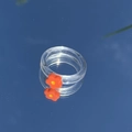 Detail eines transparenten Harzrings mit oranger Blume, gespiegelt auf Glas - Orange