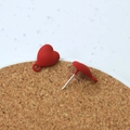 Matte red heart earrings with silver studs displayed on a round cork tray backdrop - Red