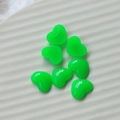 Macro detail of seven fluorescent green resin heart charms on a white textured ceramic dish - Green Heart