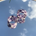 Gros plan de bagues en résine à damier violet et blanc reflétant le ciel bleu sur un miroir - Violet