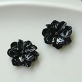 Makroaufnahme glänzender schwarzer Blumenohrstecker auf weißer Keramikoberfläche - Schwarz