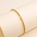 Detail eines Goldperlenarmbands mit rechteckigem klarem Stein auf weißem Papierhintergrund - Februar