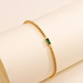 Detail eines Goldperlenarmbands mit einem rechteckigen smaragdgrünen Geburtsstein - Januar