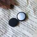 Detail of two black fabric-covered round buttons with silver metal back on vintage paper - Black