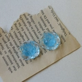 Makroaufnahme von zwei blauen Harzrosen mit Glitzer für DIY-Schmuck auf einem Vintage-Buch - Blau