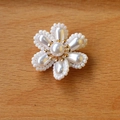 Dettaglio di ciondolo a fiore in perle fatto a mano con centro dorato su legno - Oro rosa