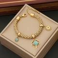Pulsera de cuentas doradas con trébol de turquesa y sol sobre joyero de color beige - Pulsera Dorada