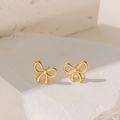 Minimalist golden bow stud earrings in polished titanium steel on a white stone background - Gold Earrings
