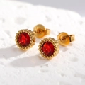 Gros plan de boucles d'oreilles en zircon rouge avec bords dorés sur pierre texturée blanche - Rond Rouge