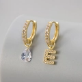 Detail van gouden huggie oorbellen met peervormige zirkoon en kristallen letter E bedel - Koper / Goud-Letter E