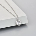 Elegante zilveren hartjesketting met glanzende zirkoonsteen op een moderne grijze display - Witte Zirconia Hart (KXL019)