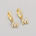 Close-up of golden hoop earring with letter M pendant and shimmering cubic zirconia stones - Gold / M