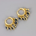 Dettaglio di orecchini a cerchio dorati con cinque pietre di zircone blu scuro pendenti - Huggie Nappa Zirconia Blu