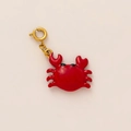 Detailed view of a red enamel crab pendant charm with a golden spring clasp on off-white - Crab