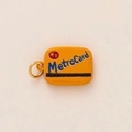 Nahaufnahme des gelben MetroCard Schlüsselanhängers mit blauem Text und Goldring - Gelber Kartenstil