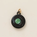 Macro view of round black enamel pendant featuring a green spiral pattern and gold jump ring - Black Plate