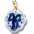 Detalle macro del colgante de corazón de cerámica blanca con lazo azul y enganche dorado - Borde Blanco Lazo Azul