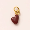 Detailed macro view of deep red heart charm with polished gold-plated double ring attachment - July Heart Pendant