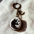 Close-up of vintage bronze keychain with painted animal pendant and moon charm on fabric - Wolf