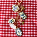 Porte-clés doré avec pendentifs fleurs et fruits sur un fond à carreaux rouge et blanc - Pendentif Petite Fleur Bleue