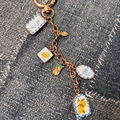 Gros plan du porte-clés doré avec pendentifs fruits et fleurs sur tissu denim - Pendentif Mangue