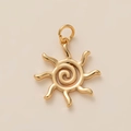 Détail d'un pendentif soleil doré avec centre en spirale et rayons ondulés sur fond beige - Soleil