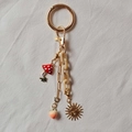 Détail d'un porte-clés doré 18K avec pendentifs champignon, pêche et soleil en relief - Soleil Pêche Champignon Rouge
